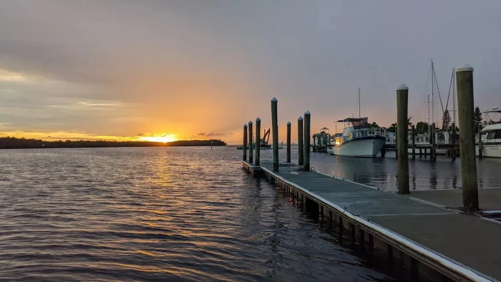 Sunset over a calm marina, with boats and a wooden dock.